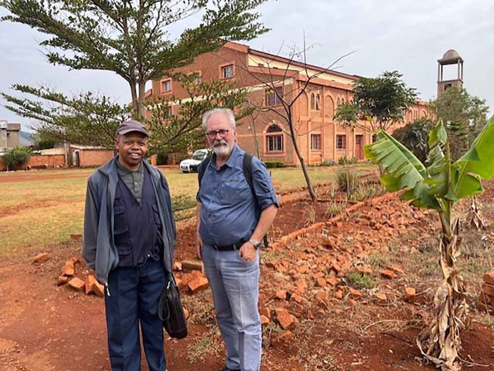 le Dr Joël Bessière et le Père Joseph devant le bâtiment principal du centre universitaire des Jésuites, dont les travaux sont en cours de réalisation.